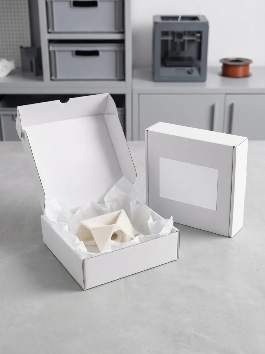 Pieza impresa envuelta en papel kraft dentro de una caja de cartón lista para enviar.